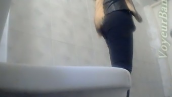 Slender white stranger girl in the toilet room shows her ass on voyeur cam
